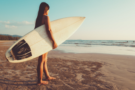 Surfer woman in bikini go to surfing. beautiful sexy woman with surfboard on beach at sunset. vintage color toneの写真素材