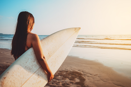 Surfer woman in bikini go to surfing. beautiful sexy woman with surfboard on beach at sunset. vintage color tone
の写真素材