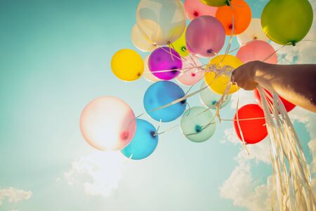 Hand holding multi colored balloons done with a retro vintage photo filter effect.の写真素材