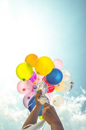 Hand holding multi colored balloons done with a retro vintage filter effect.の写真素材