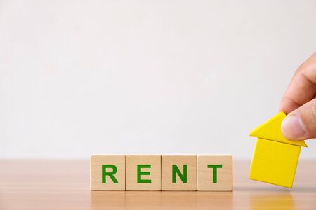 Property investment and house mortgage financial concept. Hands holding wooden house and wood cube block with RENT word.の写真素材