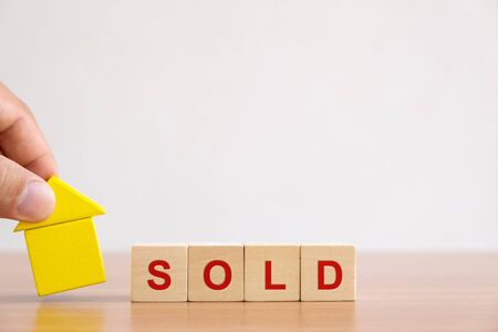Property investment and house mortgage financial concept. Hands holding wooden house and wood cube block with SOLD word.の写真素材