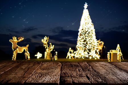 Landscape courtyard of Christmas tree with decoration, light at night in Christmas and New Year holiday. ready empty top wood table for your product display or montage.の写真素材