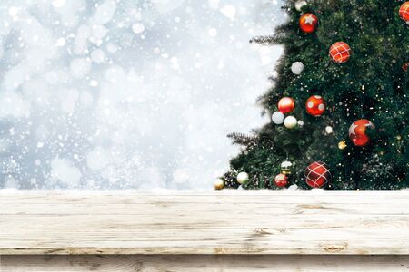 Top of empty wood table with beautiful Christmas tree and snowfall  backdrop. ready for your product display or montage. Concept of background in Christmas and New year holidays.の写真素材