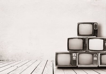 Retro televisions pile on floor in old room with white wall. Antique and vintage home decoration style. monochrome sepia photo.の写真素材