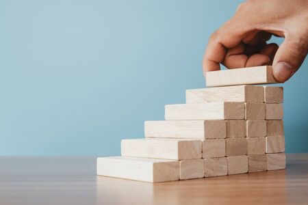 Business concept of ladder career path and growth success process. Hands of men arranging wood cube block stacking as step stair.の写真素材
