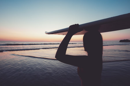 Silhouette of beautiful sexy surfer female with surfboard on the sandy beach at sunset. water sports. Surfing are healthy active lifestyle. Summertime vacation.の写真素材