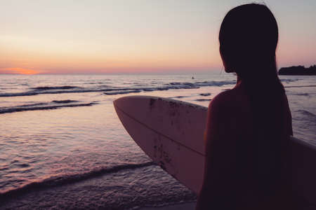 Silhouette of beautiful sexy surfer female with surfboard on the sandy beach at sunset. water sports. Surfing are healthy active lifestyle. Summertime vacation.の写真素材