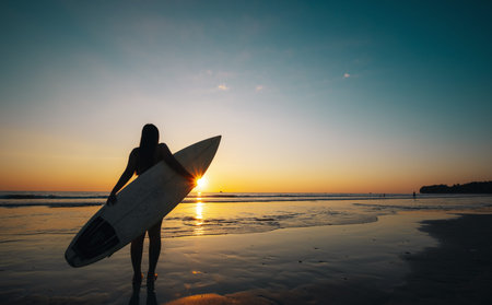 Silhouette of beautiful sexy surfer female with surfboard on the sandy beach at sunset. water...
