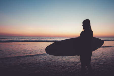 Silhouette of beautiful sexy surfer female with surfboard on the sandy beach at sunset. water sports. Surfing are healthy active lifestyle. Summertime vacation. retro color effect.の写真素材