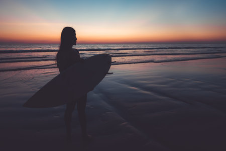 Silhouette of beautiful sexy surfer female with surfboard on the sandy beach at sunset. water...