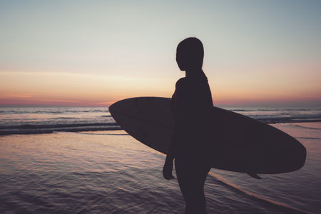 Silhouette of beautiful sexy surfer female with surfboard on the sandy beach at sunset. water sports. Surfing are healthy active lifestyle. Summertime vacation. retro color effect.の写真素材