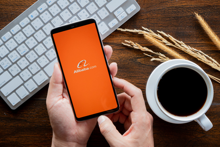 Chiang Mai / Thailand - jan 20 2019 : Hands hoding mobile with Alibaba screen, Coffee and keyboard on wood deskのeditorial素材