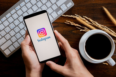 Chiang Mai / Thailand - jan 20 2019 : Hands hoding mobile with instagram screen, Coffee and keyboard on wood deskのeditorial素材