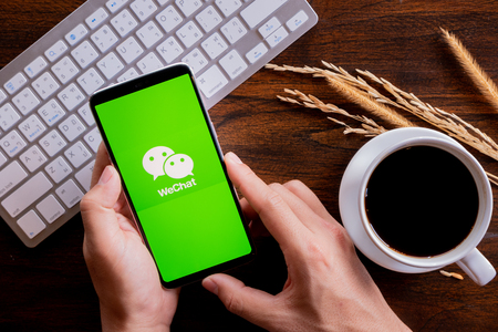 Chiang Mai / Thailand - jan 20 2019 : Hands hoding mobile with wechat screen, Coffee and keyboard on wood deskのeditorial素材