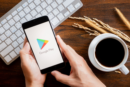 Chiang Mai / Thailand - jan 20 2019 : Hands hoding mobile with google play screen, Coffee and keyboard on wood deskのeditorial素材