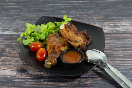 Grilled chicken on wooden board with sauce and tomatoの写真素材