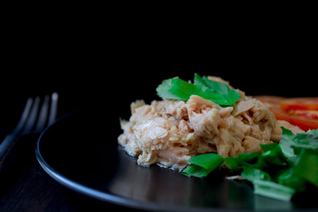 Tuna salad placed on a black plate with a side dish on a black background is a healthy food that...