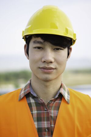 Front view of a young Asian engineer wearing reflective Orange clothing looks serious and happy. He standing on the construction project.And copy space.の写真素材