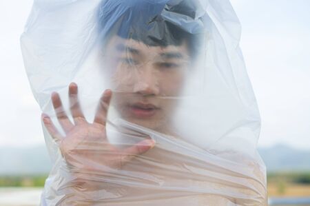 Asian gay man is wearing a plastic bag on his head that has suffocated a concept to stop using plastic and environmental pollution or stops marine and world pollution.And copy space.の写真素材