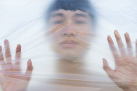 Asian gay man is wearing a plastic bag on his head that has suffocated a concept to stop using plastic and environmental pollution or stops marine and world pollution.And copy space.の写真素材