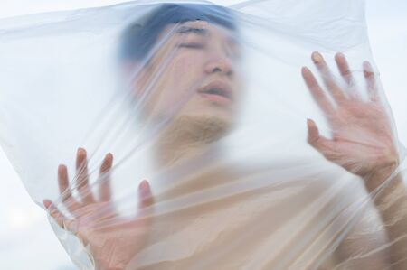 Asian gay man is wearing a plastic bag on his head that has suffocated a concept to stop using plastic and environmental pollution or stops marine and world pollution.And copy space.の写真素材