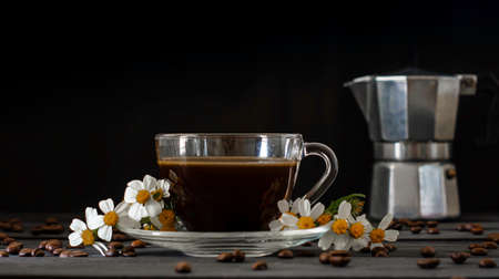 Hot coffee in a coffee cup and roasted coffee beans with flowers beside the cup on a dark tone wood floor and copy space.の写真素材