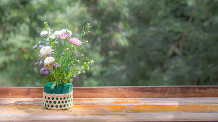 Flowers in a basket placed on a wooden table with natural sunlight spreading thin and copy space.の写真素材