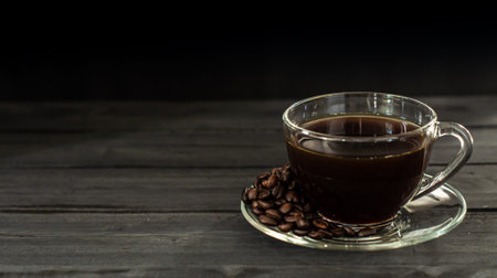 Hot coffee in a coffee cup and roasted coffee beans with a dark tone wood floor. And there is a copy space.の写真素材