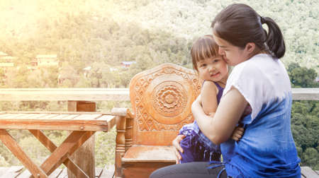 Closed up Asian mother carried her child and kissed her childhood daughter happily with the orange evening light in the backyard.の写真素材
