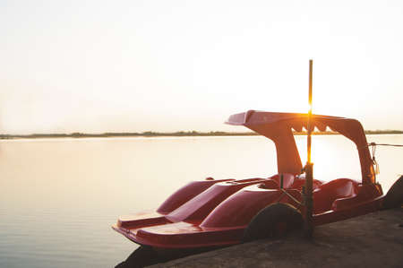 A red spinning boat is moored by the lake during the warm evening sun, with the sun shining from the back of the boat.の写真素材