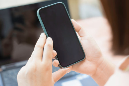 Asian woman's hand holding a smartphone and finger touching the blank screen. Sit outside with natural light.の写真素材
