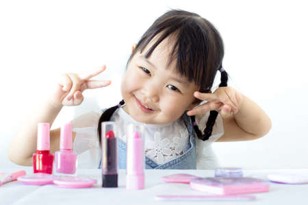 A cute Asian girl is enjoying her makeup with makeup on the table. The back has a white background.の写真素材