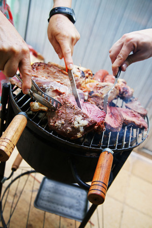 Several hands are handling and cutting glazed barbecue meat steaks from veal and lambの写真素材