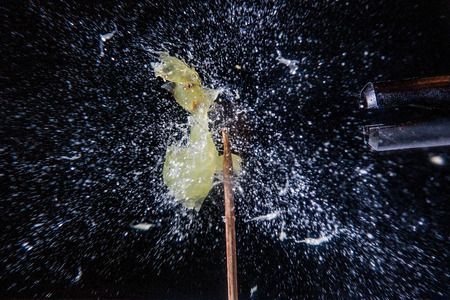 A green grape being shot and exploding in a burst of water on black backgroundの写真素材