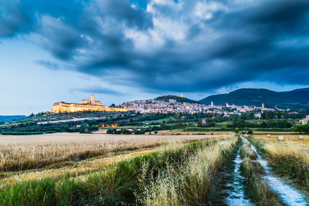 Beautiful view of the ancient town of Assisi with dramatic cloudscape during blue hour, Umbria, Italyの写真素材