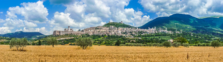 Panoramic view of the ancient town of Assisi with dramatic cloudscape and golden harvest fields, Umbria, Italyの写真素材