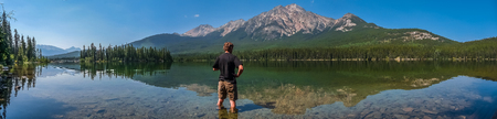 Beautiful panoramic view of lonely man standing in Pyramid Lake with great mountain landscape in the background, Jasper National Park, Alberta, Canadaの写真素材