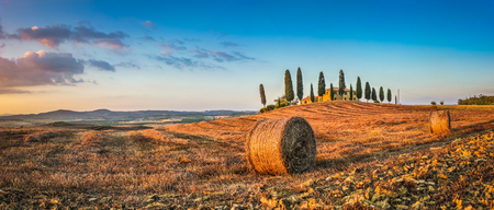 Panoramic view of beautiful Tuscany landscape with traditional farm house and hay bales in golden evening light, Val d'Orcia, Italyの写真素材