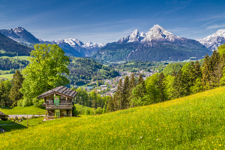 Panoramic view of idyllic mountain landscape in the Alps with fresh green mountain pastures with flowers and old traditional mountain lodge in springtimeの写真素材