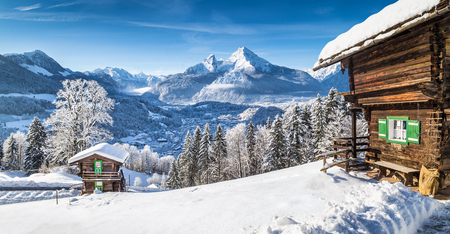Winter wonderland mountain scenery in the Alps with traditional mountain chalets on a cold sunny day with blue sky and cloudsの写真素材