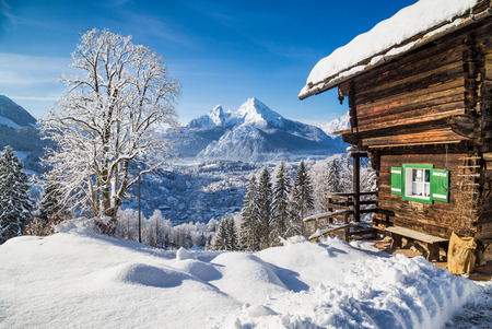 Winter wonderland mountain scenery in the Alps with traditional mountain chalet on a cold sunny day with blue sky and clouds