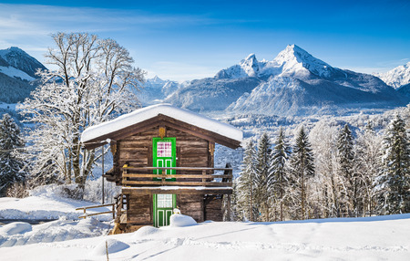 Panoramic view of beautiful winter wonderland mountain scenery in the Alps with traditional mountain chalet on a cold sunny day with blue sky and cloudsの写真素材