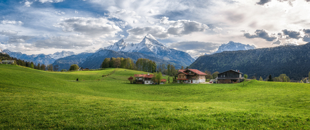 Idyllic landscape in the Alps with fresh green meadows, blooming flowers, typical farmhouses and snowcapped mountain tops in the background, Nationalpark Berchtesgadener Land, Bavaria, Germanyの写真素材