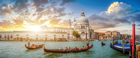 Beautiful view of traditional Gondolas on famous Canal Grande with historic Basilica di Santa Maria della Salute in the background in romantic golden evening light at sunset in Venice, Italyの写真素材