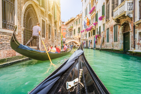 Traditional gondolas on narrow canal in Venice, Italy with retro vintage toned style grunge filter and lens flare sun light effect on a sunny day with blue sky in summerの写真素材