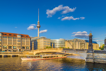 Beautiful view of famous TV tower and historic buildings at Museum Island with boat passing Friedrichsbruecke on Spree river in golden evening light with blue sky at sunset in summer, Berlin, Germanyの写真素材