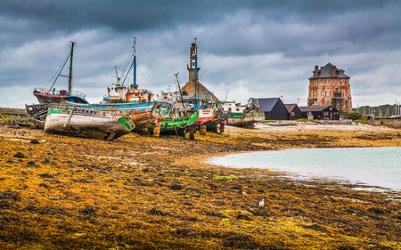 Beautiful view of old abandoned shipwrecks lying on a beach with dark dramatic clouds in summer, commune of Camaret-sur-Mer, Bretagne, northwestern Franceの写真素材