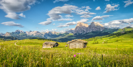 Panoramic view of idyllic alpine mountain scenery with traditional old mountain chalets and fresh green meadows in beautiful golden evening light at sunset in summer, Alpe di Siusi, South Tyrol, Italyの写真素材