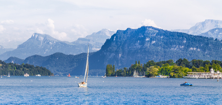 Scenic panoramic view of boats on idyllic Lake Lucerne with alpine mountain scenery in the background on a beautiful sunny day with blue sky and clouds in summer, Lucerne, Switzerlandの写真素材